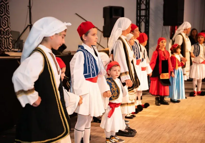 Kinder in Fustanella und Trachtenkleidern stehen in einer Reihe auf der Bühne
